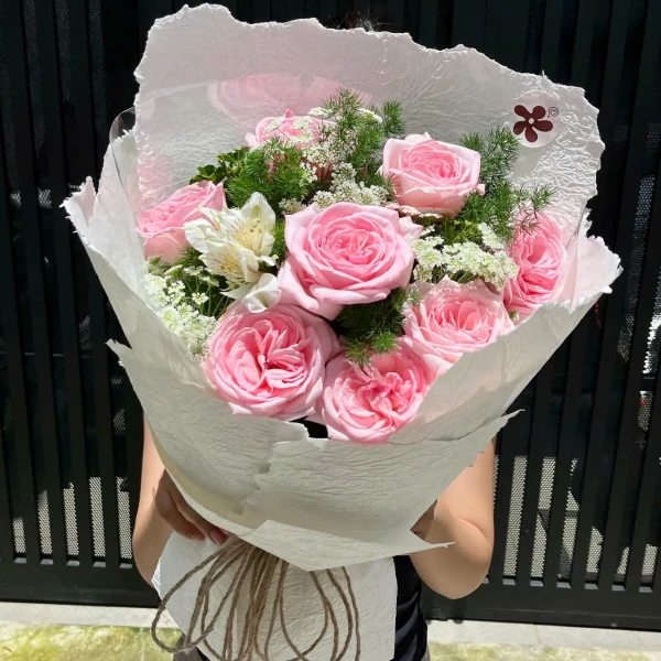 Pink roses and white alstroemeria in a white bouquet wrap, tied with twine.