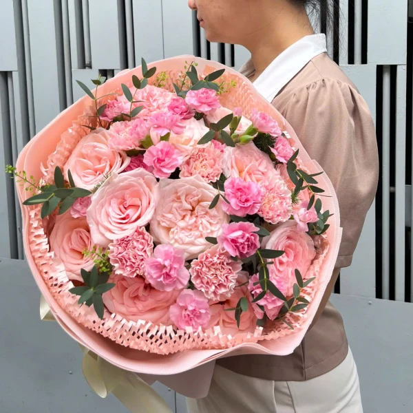 Pink roses and carnations arranged in a bouquet with light pink paper and ribbon.
