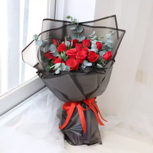 A bouquet of 18 red roses, wrapped in black paper and tied with a red ribbon.
