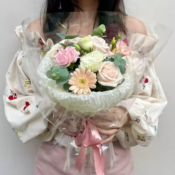 Woman holding a pink and white flower bouquet wrapped in clear plastic with a pink bow.