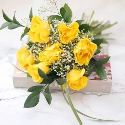 Bouquet of yellow roses and baby's breath with green leaves on a box.