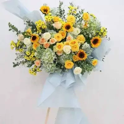 A grand floral arrangement with sunflowers, roses, and hydrangeas in yellow and light blue wrapping.