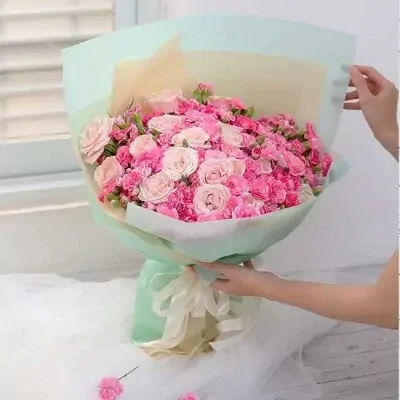 A large bouquet of pink roses and carnations wrapped in mint green paper and tied with a cream ribbon.