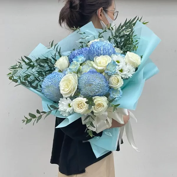 Bouquet of blue chrysanthemums, white roses, and greenery wrapped in light blue paper.