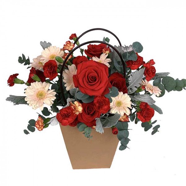 Red roses, gerbera daisies, and carnations in a brown basket with dark handles.