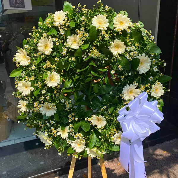 White gerbera daisies and white aster flowers arranged in a wreath with a white bow.