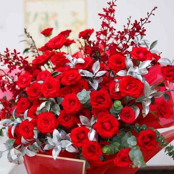 A bouquet of red roses, red orchids, and silver leaves in a red vase.