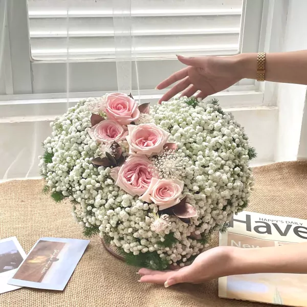 Pink roses and baby's breath in a heart-shaped arrangement, with hands reaching out.
