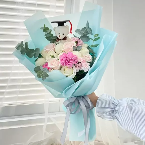 Graduation bouquet with a teddy bear in a cap, pink and white roses, carnations, and eucalyptus.