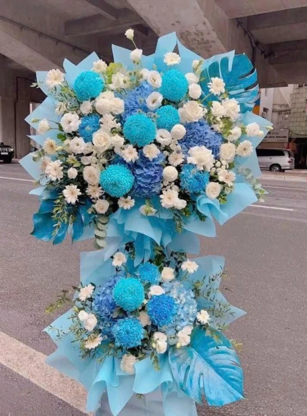 Two blue and white floral arrangements with blue monstera leaves.