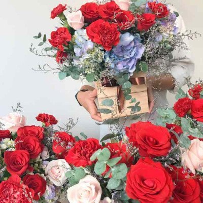 A wooden box filled with red roses, red carnations, and blue hydrangeas.