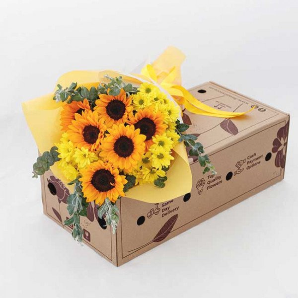 Bright yellow sunflowers and yellow chrysanthemums arranged in a bouquet with eucalyptus in a cardboard box.
