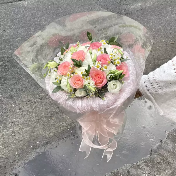 Pink and white roses and other flowers in a bouquet with a pink ribbon.