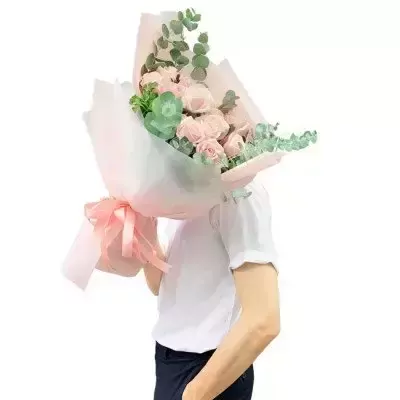 A bouquet of light pink roses, succulents, and eucalyptus leaves wrapped in light pink paper with a matching ribbon.