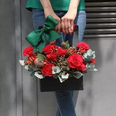 Black flower basket with red roses and carnations, tied with a green bow.