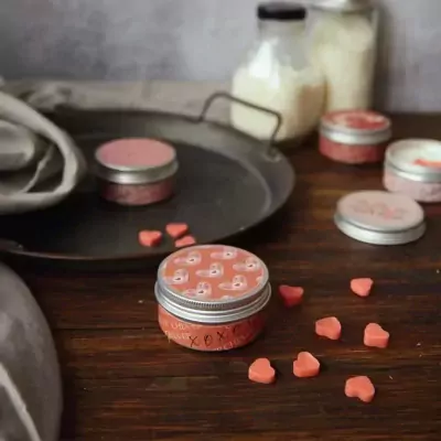 Pink scented candles with heart-shaped wax melts, on a wooden surface.