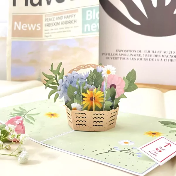 Pop-up card with a 3D basket of colorful flowers and a newspaper in the background.