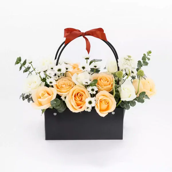 Orange and white roses in a black basket with a red bow.