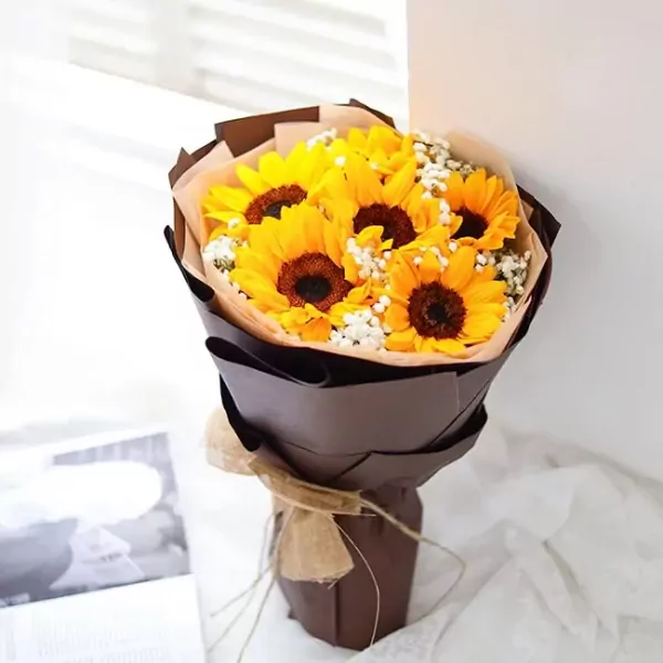 Bouquet of bright yellow sunflowers and baby's breath in brown paper wrapping, tied with twine.