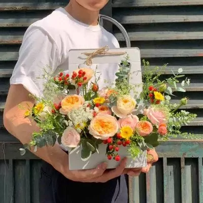 Person in white shirt holding a rectangular floral arrangement with roses and greenery.