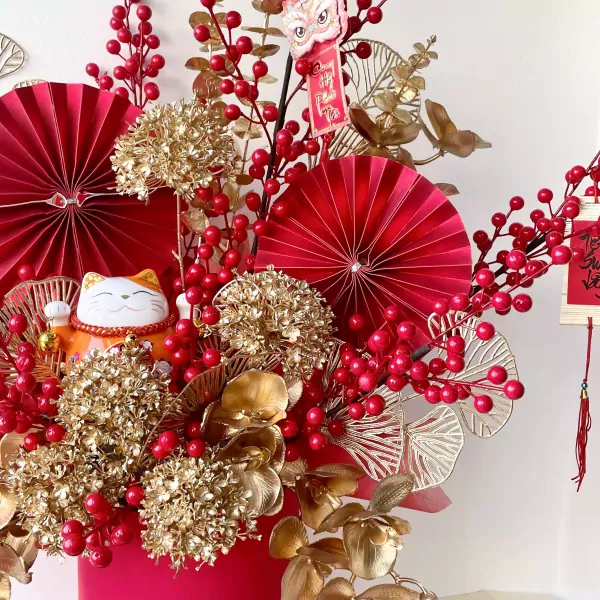 Maneki-neko cat with red and gold floral arrangement, red fans, and berries.