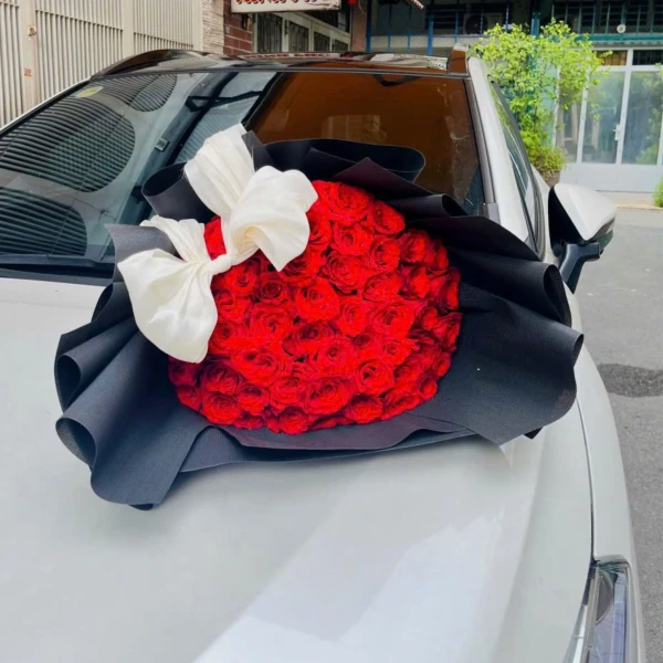 Bouquet of 50 red roses with a white bow on black wrapping.