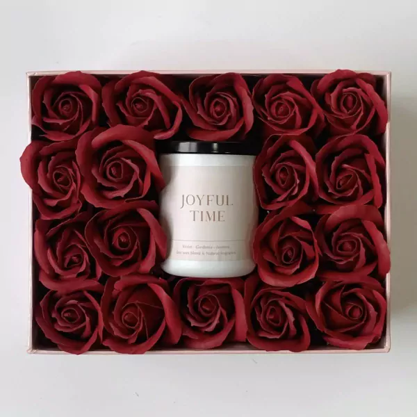 Red roses surround a candle with "JOYFUL TIME" label in a rose gold gift box.