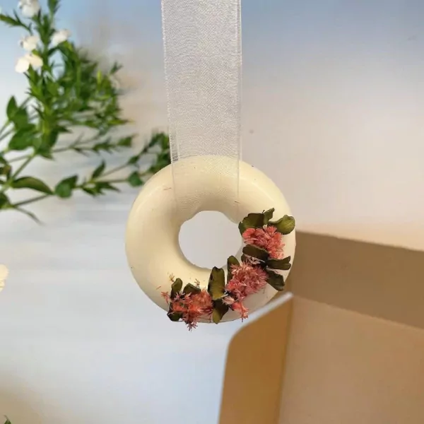 White donut-shaped wax ornament with pink dried flowers, hanging by a ribbon.