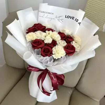 A bouquet of red roses and white carnations wrapped in white paper, tied with a red ribbon.
