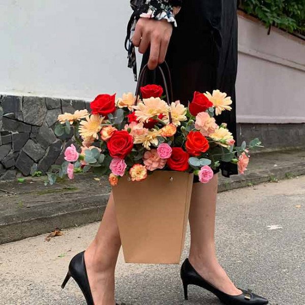 Woman in black dress and heels carries a brown floral basket with red and pink roses.