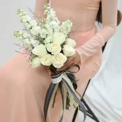 White roses and white stock flowers in a bridal bouquet, tied with a gray and white ribbon.