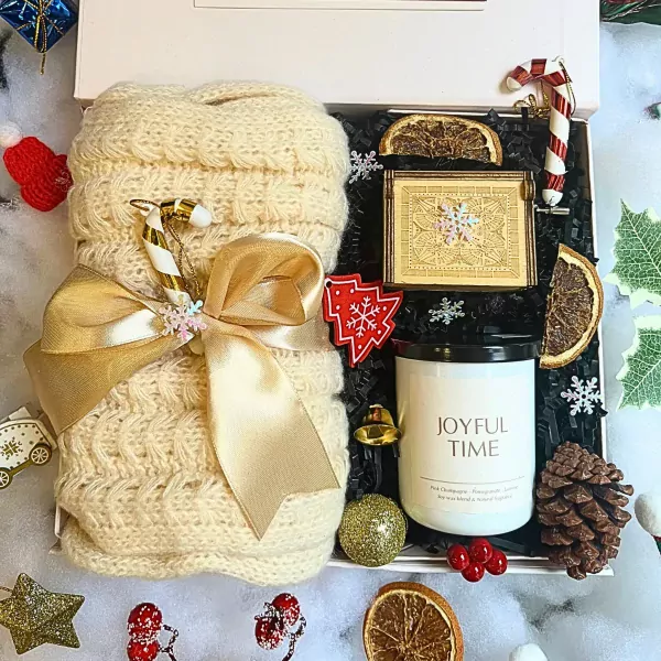 Christmas gift box with knitted scarf, candle, music box, and festive decorations.