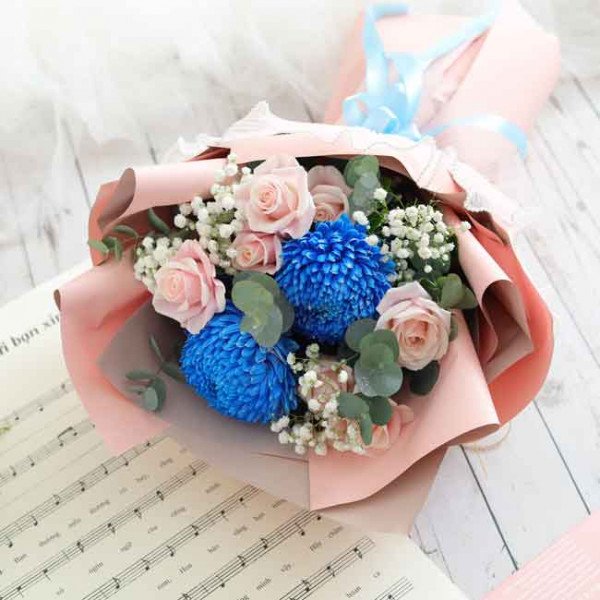 Bouquet of pink roses, blue mums, and baby's breath in pink paper with a blue ribbon.