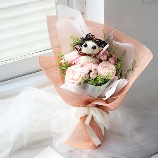 Bouquet with pink roses, daisy poms, and a stuffed toy doll.