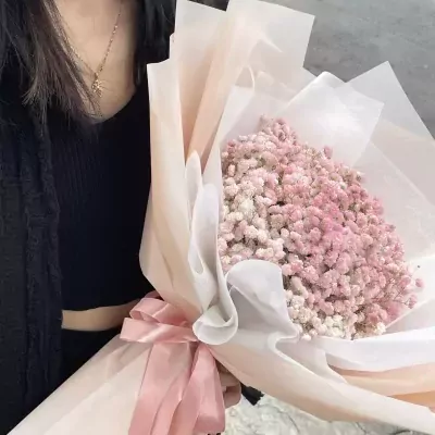Hand holding a bouquet of pink baby's breath with a satin ribbon.