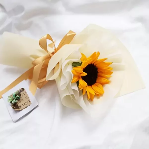 A single sunflower in a bouquet of pale yellow paper, tied with a gold ribbon.