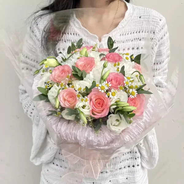 A woman holds a bouquet of pink and white roses and other flowers, wrapped in cellophane.