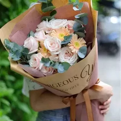 A bouquet of pink roses, gerbera daisies, and eucalyptus in kraft paper with "Gorgeous You" text.