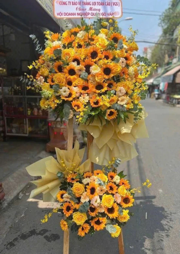 Two tiered floral arrangement with sunflowers, yellow roses, and other yellow flowers.