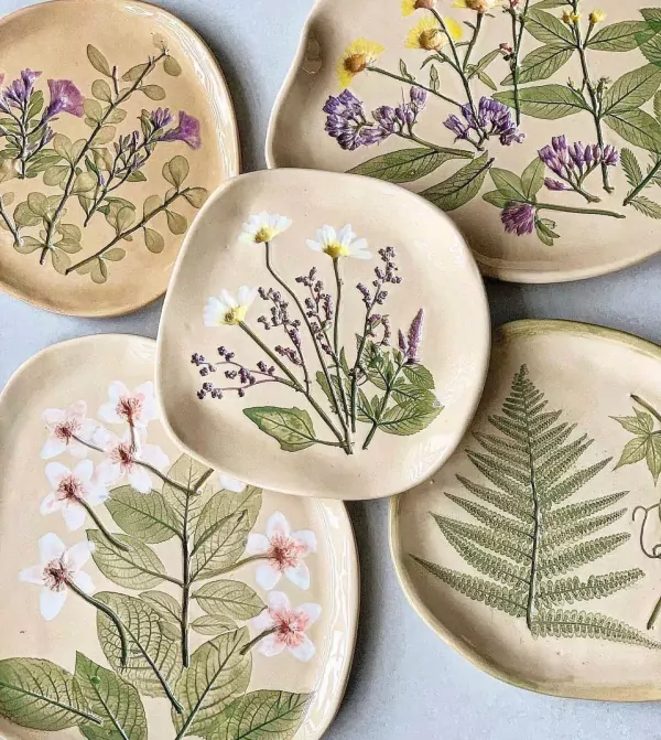 Ceramic plates with pressed flowers and leaves, including ferns and daisies.