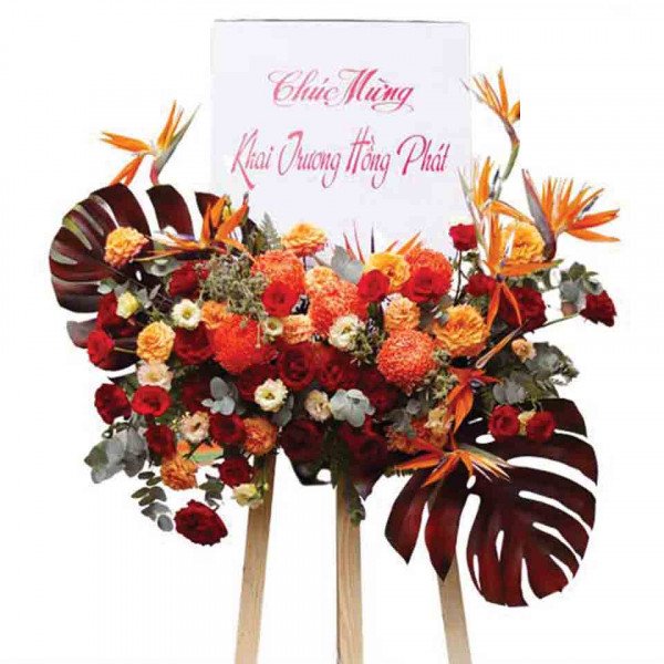 Floral arrangement for opening ceremony with red and orange roses, chrysanthemums, and tropical leaves.