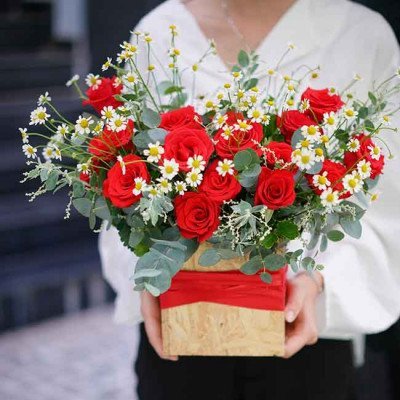 Red roses and white daisies in a wooden box with red ribbon.