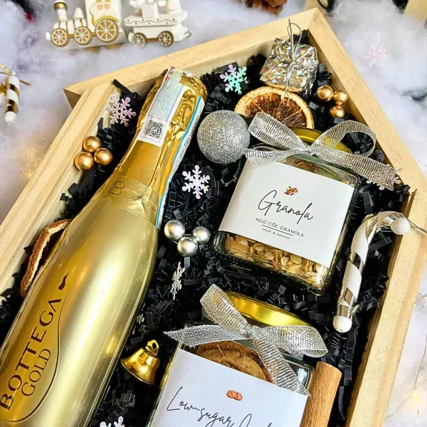 Christmas gift box with champagne, granola, cookies, and festive decorations.