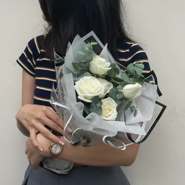 Bouquet of white roses and eucalyptus, wrapped in sheer white and black paper.