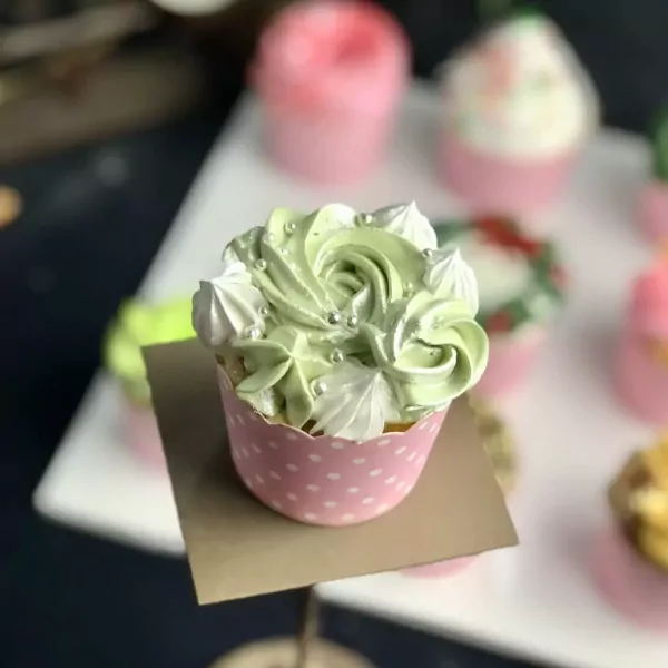 A pale green cupcake decorated with swirls of frosting, meringues, and silver sprinkles.
