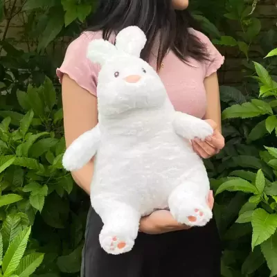 White plush rabbit with pink paw pads, held by a person in a pink shirt amidst green foliage.