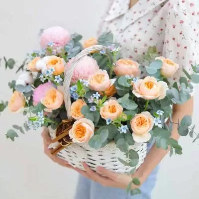 Basket of pink peonies, orange David Austin roses, and blue flowers with eucalyptus.