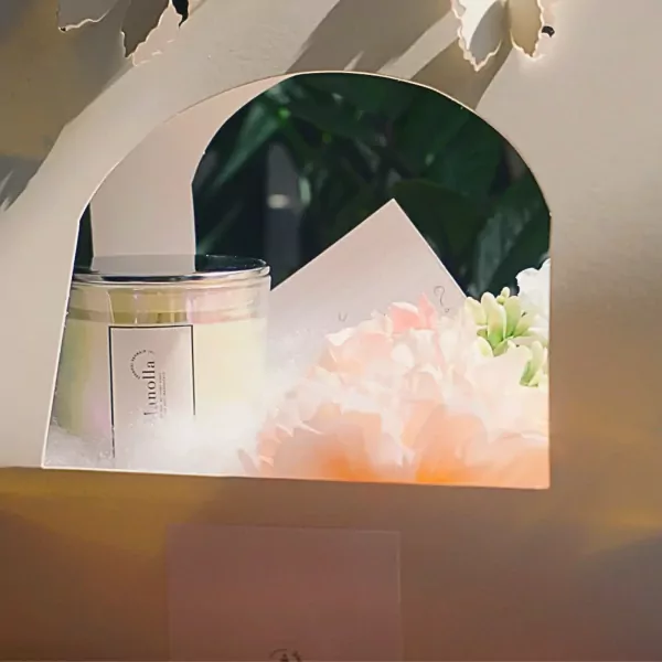 A scented candle with delicate pink and white flowers in an arched gift box.