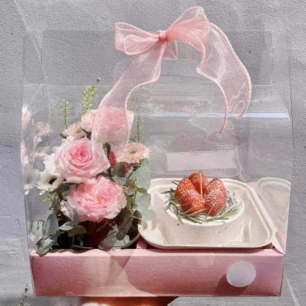 Floral gift box with pink roses, greenery, and a small cake topped with strawberries.