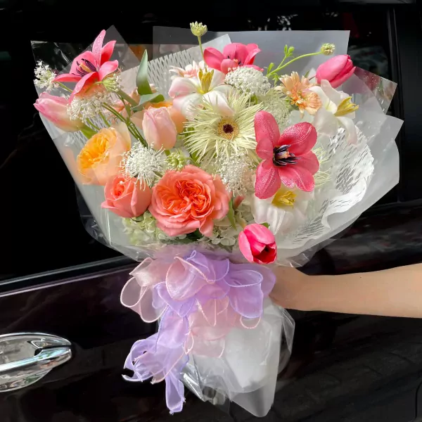 A hand holds a bouquet of pink and orange flowers with a sheer ribbon.